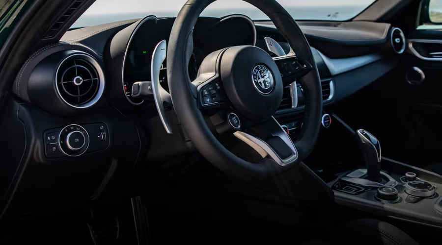A close-up of a driver's hand selecting GPS navigation route alternatives on the sleek, integrated 8.8-inch center touchscreen inside a 2026 Alfa Romeo Giulia