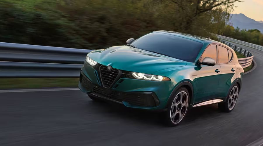 Green 2026 Alfa Romeo Tonale navigating a winding autumn highway curve along Route 17 near Ramsey, NJ, demonstrating Q4 All-Wheel Drive stability on wet local roads.