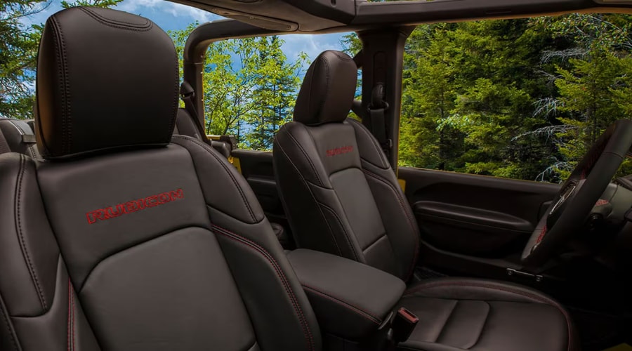 Dark leather front bucket seats with red embroidered Rubicon lettering, contrast red stitching, and open-air view of autumn trees inside a 2026 Jeep Gladiator Rubicon near Ramsey, NJ.