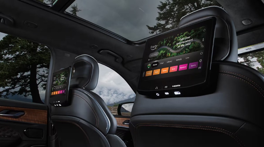 The premium dual rear-seat entertainment screens of a 2026 Jeep Grand Cherokee shown in image_9801f5.jpg, featuring built-in Fire TV displays mounted on the back of the front leather seats under a wide panoramic sunroof near Monsey