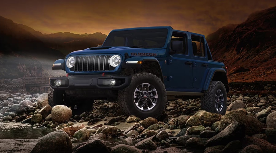 A blue 4-door 2026 Jeep Wrangler Rubicon navigating rocky terrain in North Jersey, showcasing all-weather visibility and rugged off-road performance.