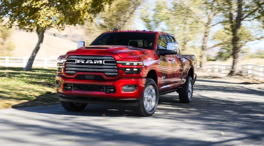 Front three-quarter action shot of a bright red 2026 Ram 2500 Heavy-Duty truck driving smoothly down a paved road, highlighting chrome grille accents, LED lighting, and cab clearance lights for truck buyers in Ramsey, NJ and Bergen County.
