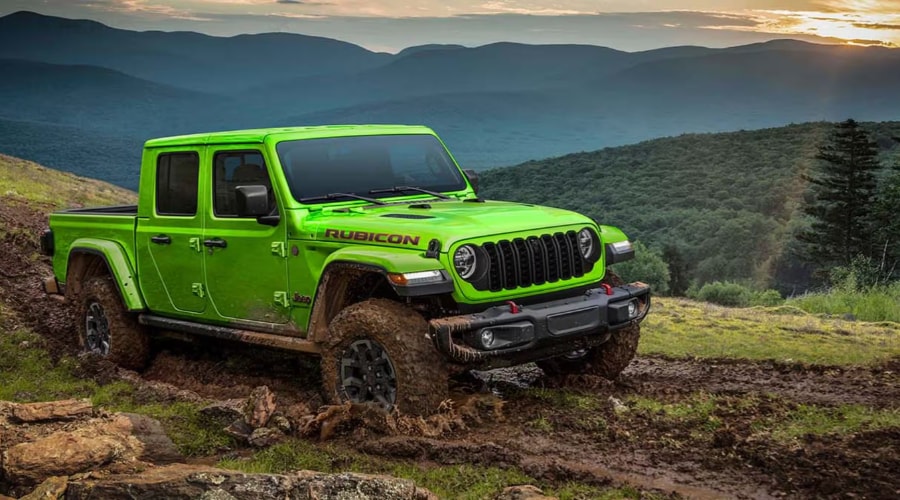 Bright lime green 2026 Jeep Gladiator Rubicon 4x4 pickup truck navigating a muddy mountain trail at sunset near Ramsey, NJ, demonstrating off-road traction, mud-terrain tires, and red front tow hooks.