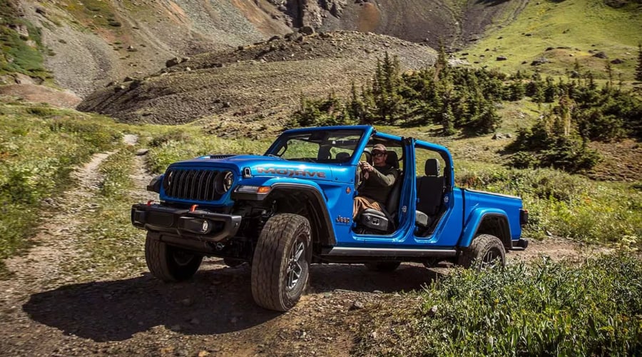A bright blue 2026 Jeep Gladiator Mojave navigating a steep, rocky trail with the doors off, demonstrating 2026 Jeep Gladiator performance and open air 4x4 utility pickup capability for off-road buyers in Ramsey and Mahwah, NJ