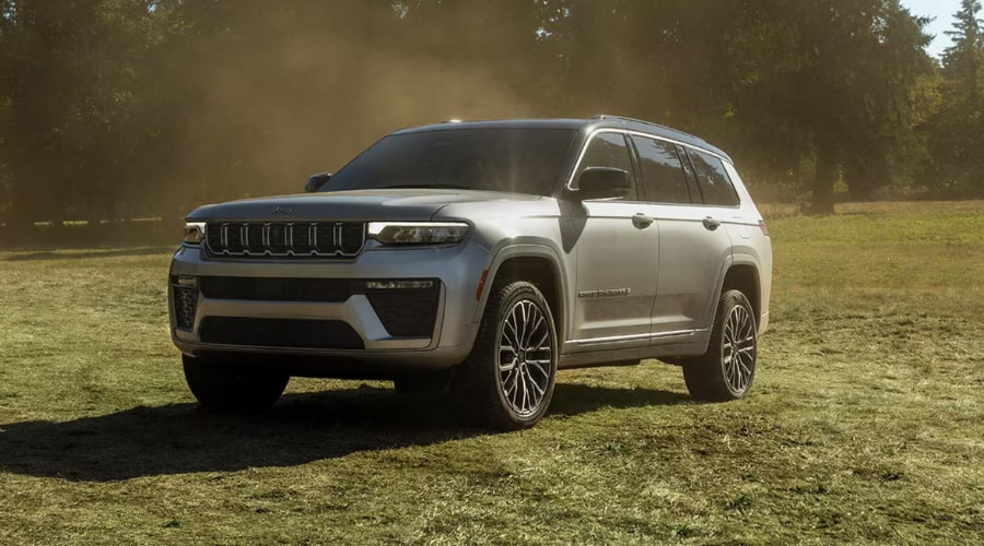 Silver 2026 Jeep Grand Cherokee SUV parked in a sunlit field with trees in the background, illustrating summer heat protection and engine cooling maintenance for drivers in Bergen County, NJ
