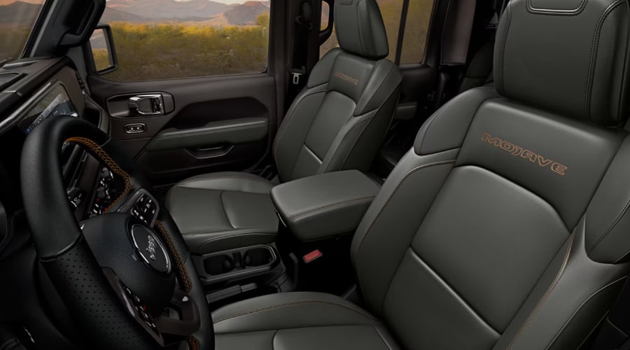 Interior cab of a 2026 Jeep Gladiator Mojave featuring dark leather front bucket seats with orange Mojave embroidery, contrast stitching, and climate control console for comfortable autumn commuting in Ramsey, NJ.