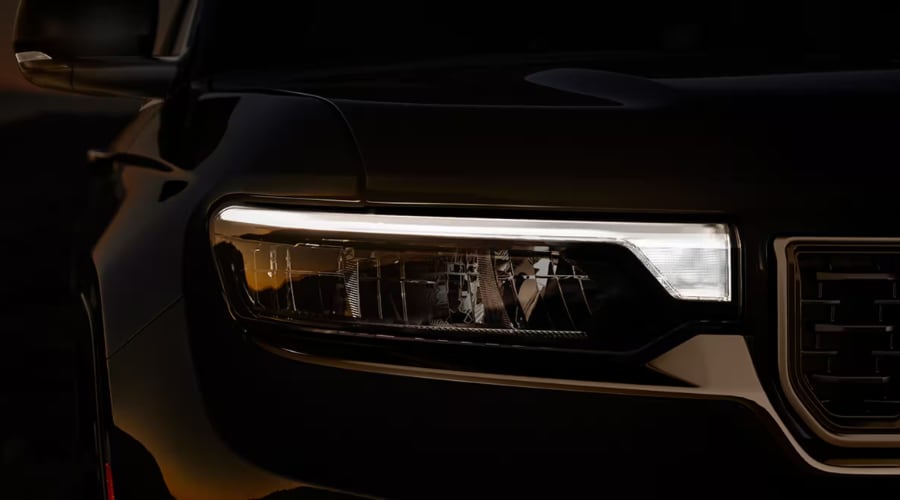 Close-up shot of the illuminated LED headlight assembly and front grille on a black 2026 Jeep Grand Cherokee SUV, highlighting lighting and electrical system care for evening Route 17 commutes in Bergen County, NJ.