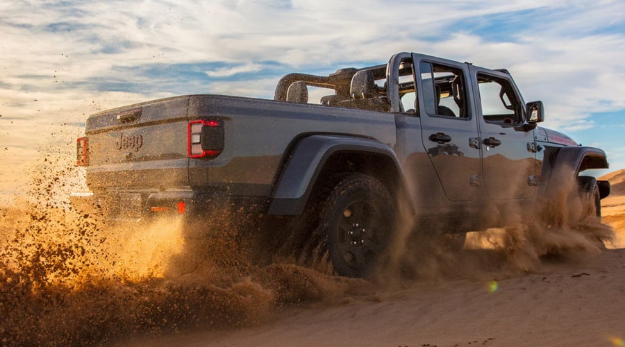 Rear view of a grey 2026 Jeep Gladiator 4WD kicking up sand, demonstrating rugged open-air performance and steel truck bed utility for midsize pickup truck drivers in Ramsey and Mahwah, NJ