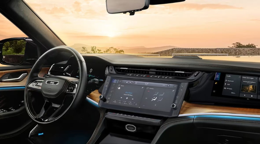 Wide view of the 2026 Jeep Grand Cherokee luxury interior cabin during sunset, featuring the digital dashboard, leather-wrapped steering wheel, and Uconnect climate control screen for autumn commute comfort in Mahwah, NJ.