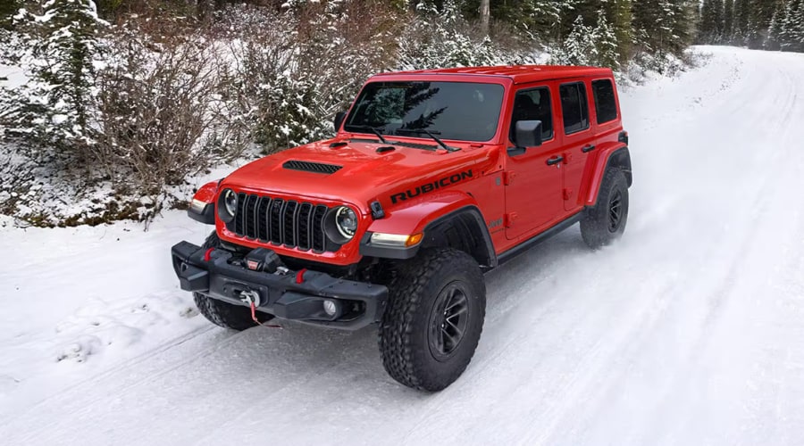 Red 2026 Jeep Wrangler Rubicon driving on a snow-covered road on a chilly morning, demonstrating cold-weather performance and clear windshield visibility near Ramsey, NJ.