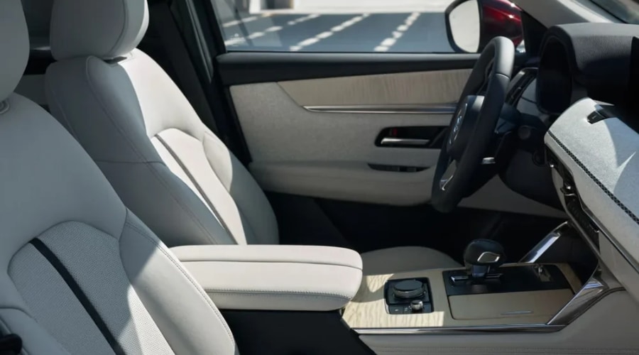 Sunlit front cabin interior of a 2026 Mazda CX-90 in Ramsey, NJ featuring light gray perforated leather seats, light maple wood center console, and Mi-Drive controls for comfortable autumn driving across Bergen County.