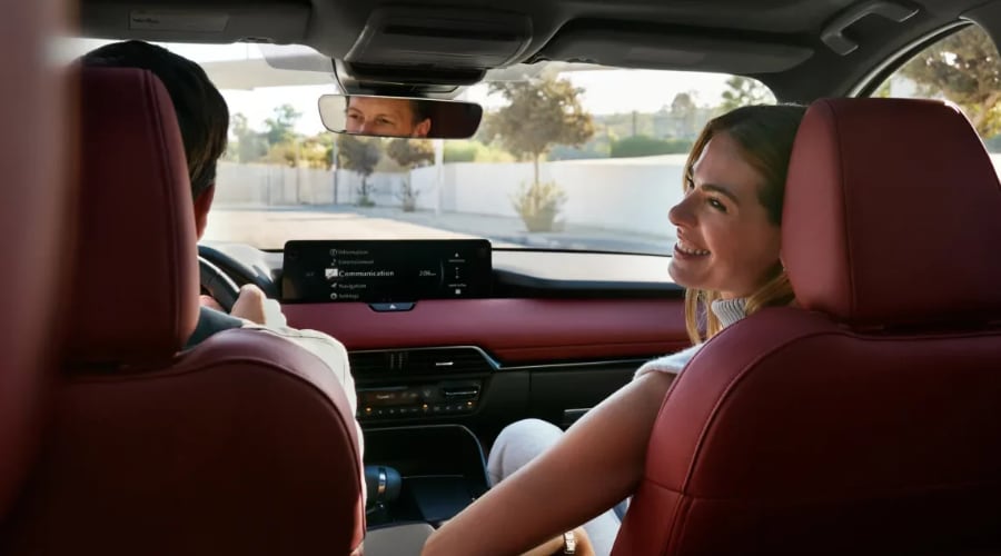 Interior view of a 2026 Mazda CX-70 featuring red leather seats and a panoramic sunroof as a couple enjoys a cozy morning drive in Ramsey, NJ, showcasing the crossover's dual-zone climate control.