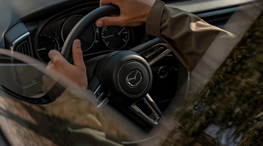 Driver holding the leather-wrapped steering wheel of a 2026 Mazda CX-50 Hybrid, using push-to-talk voice controls during a North Jersey commute