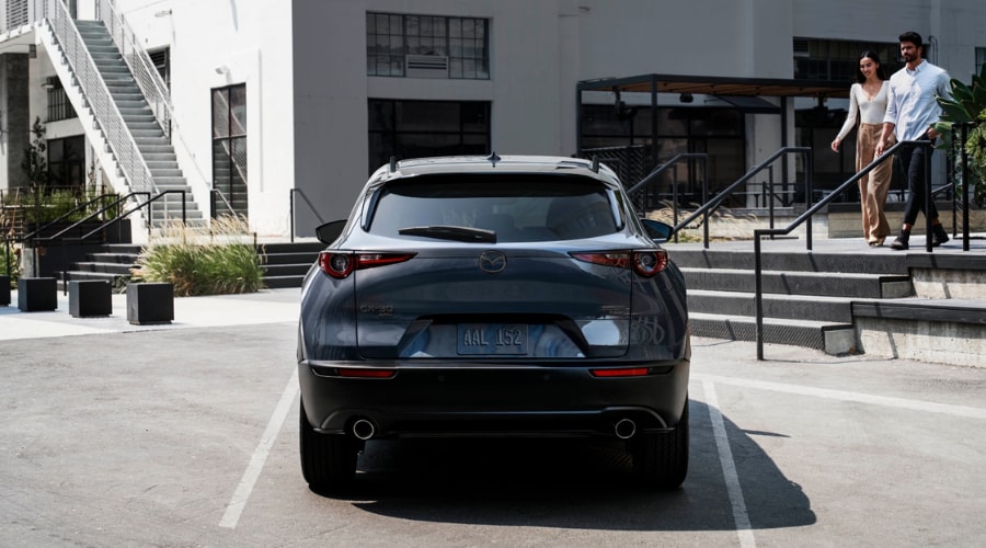 Rear exterior view of a dark grey 2026 Mazda CX-30 Turbo AWD parked near a shopping plaza, showcasing practical cargo utility and compact dimensions for young professionals in Paramus and Ridgewood, NJ.
