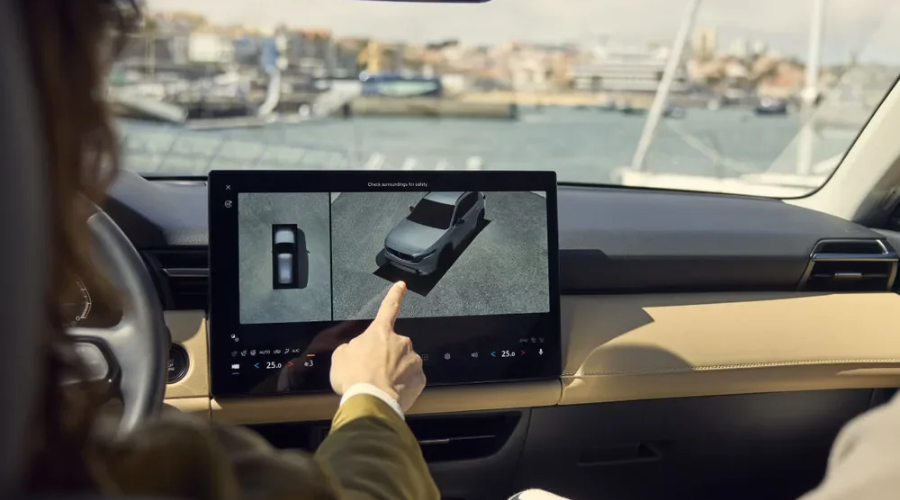 Driver operating the central touchscreen display in a 2026 Mazda CX-5 showing the 360 View Monitor camera feed, demonstrating active safety technology and cabin electronics care available at Ramsey Mazda in Bergen County, NJ