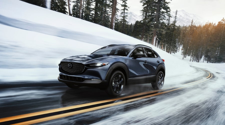 Dark blue 2025 Mazda CX-30 crossover navigating a snow-covered mountain road with i-Activ AWD and active safety features in Bergen County, NJ winter conditions.