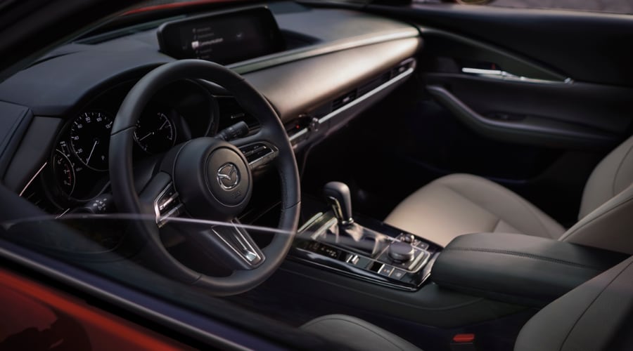 Interior driver cabin view of a red 2025 Mazda CX-30 showing steering wheel safety controls and Commander dial interface in Bergen County, NJ.