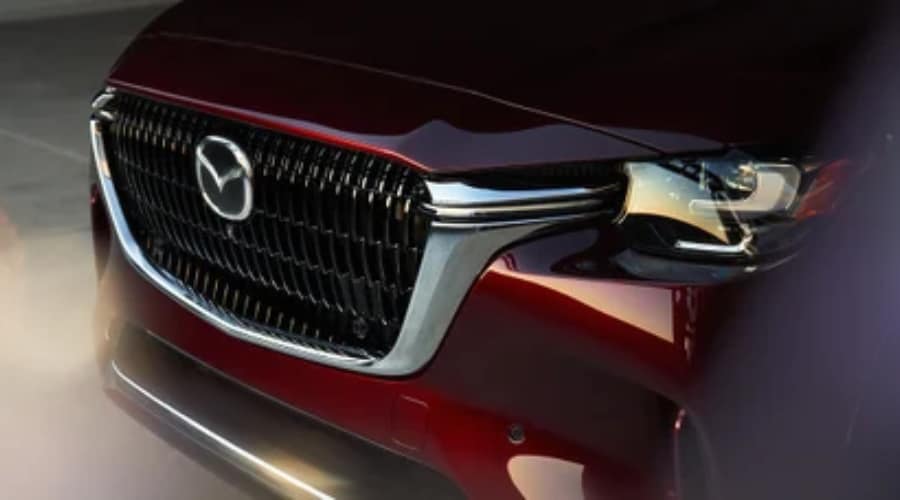 Close-up of the front grille, chrome signature wing, and LED headlight array of a 2026 Mazda CX-90 in Artisan Red at Ramsey Mazda in Ramsey, NJ.