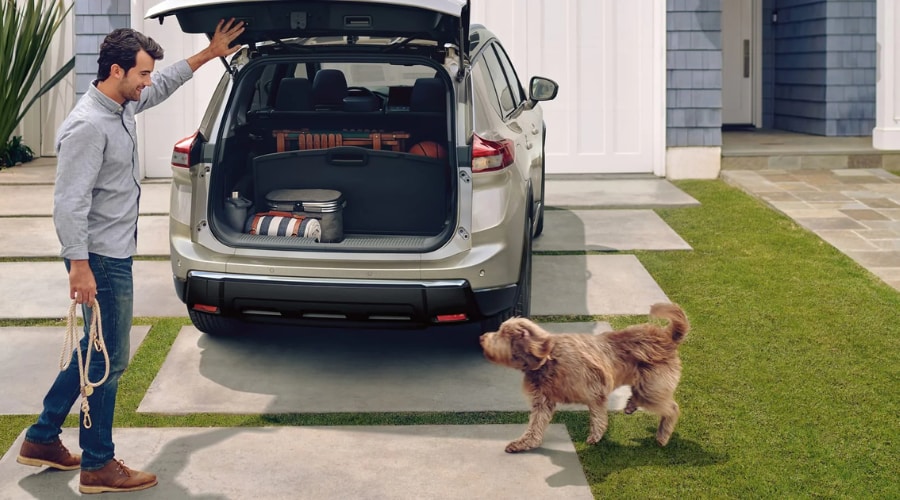 Man organizing outdoor gear in the open trunk of a 2026 Nissan Rogue using the Divide-N-Hide cargo system in a suburban Ramsey NJ driveway with his dog nearby