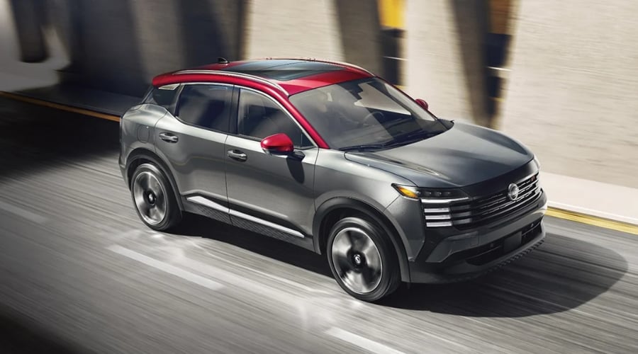 2026 Nissan Kicks compact crossover with Intelligent AWD driving on a wet, rainy highway through Bergen County, New Jersey near Ramsey and Mahwah, showcasing its gray exterior and red roof design for autumn commuters.