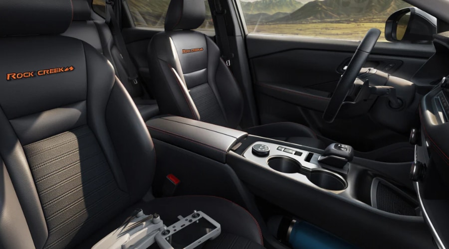 Interior front cabin view of a 2026 Nissan Rogue Rock Creek Edition featuring black water-repellent seats with orange embroidered badges, high-contrast stitching, and center console drive mode selector at Ramsey Nissan in Bergen County, NJ.