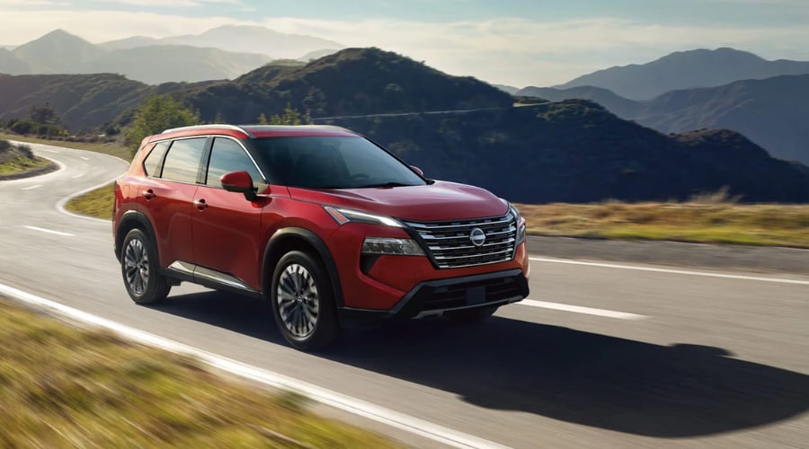 Scarlet red 2026 Nissan Rogue cruising along a curving two-lane highway, highlighting active ProPILOT Assist with Navi-link speed adjustments for commuters near Route 17 and Ramsey Nissan in Bergen County, NJ.