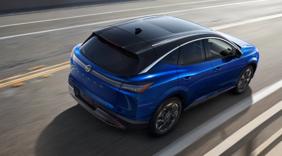 High-angle rear perspective of a two-tone metallic blue 2026 Nissan Murano Platinum driving on a multi-lane highway, highlighting Intelligent AWD utility for Bergen County, NJ commuters.