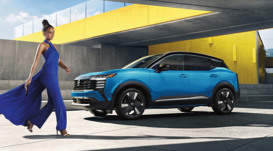 Front three-quarter view of a two-tone blue and black 2026 Nissan Kicks parked in a modern urban concrete setting with a vibrant yellow background wall, highlighting its athletic stance