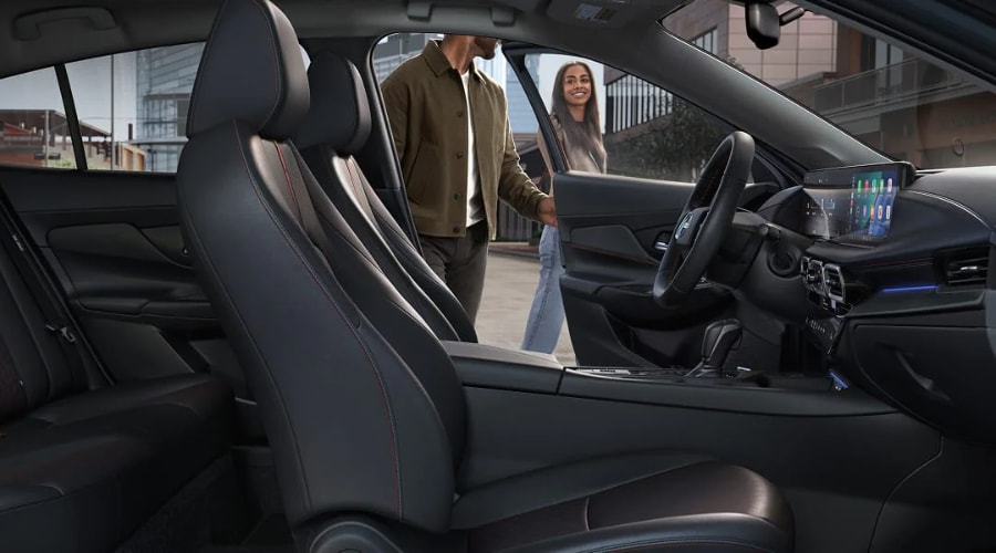 Spacious charcoal interior of the 2027 Nissan Sentra featuring sport seating with contrast stitching, a flat-bottom steering wheel, and a large digital touchscreen display, available for a test drive at Ramsey Nissan in Ramsey, NJ.