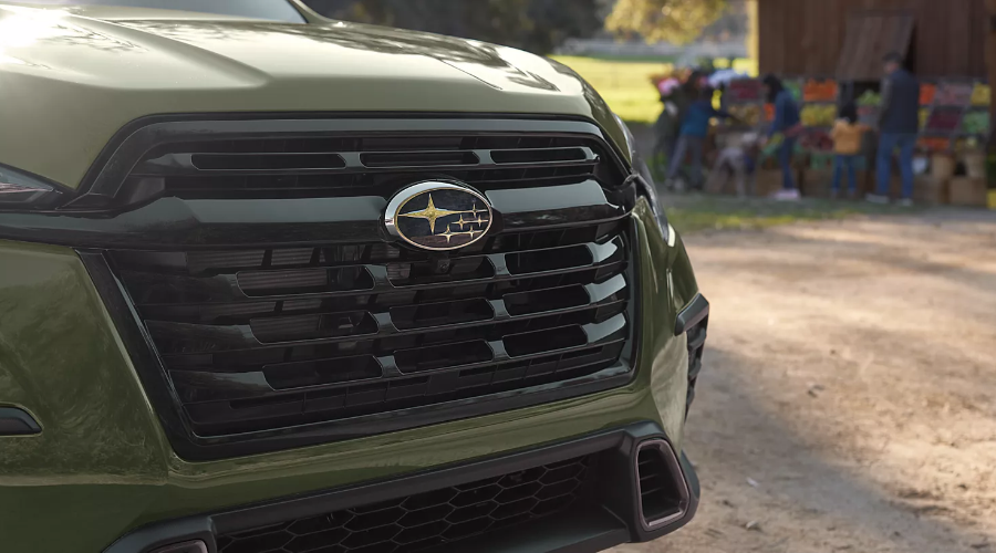 Close-up view of the bold black front grille and chrome Subaru emblem on a 2027 Subaru Ascent parked near an outdoor family farm stand in Bergen County, NJ, available at Ramsey Subaru.