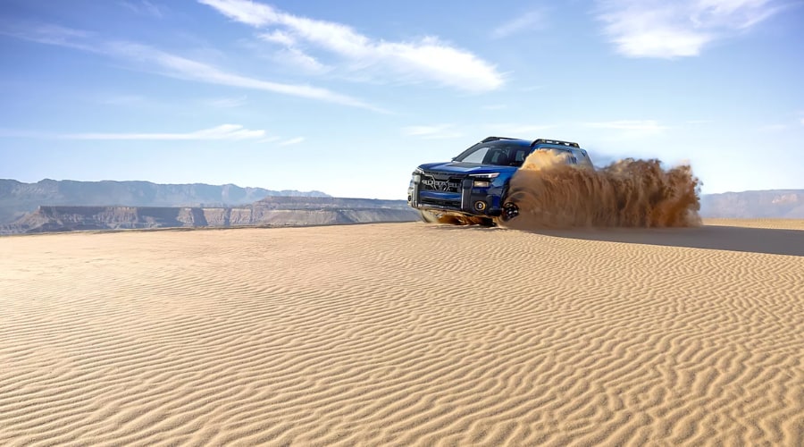 Blue Subaru Outback kicking up a spray of sand while navigating sand dunes, demonstrating Dual-Function X-MODE deep snow and mud traction control for off-road drivers near Mahwah and Ramsey, NJ.