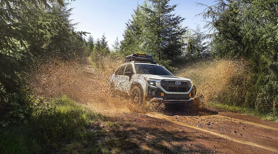 Front profile of a 2026 Subaru Forester driving through winter mud in Ramsey showing its sleek redesigned grille and standard LED headlights