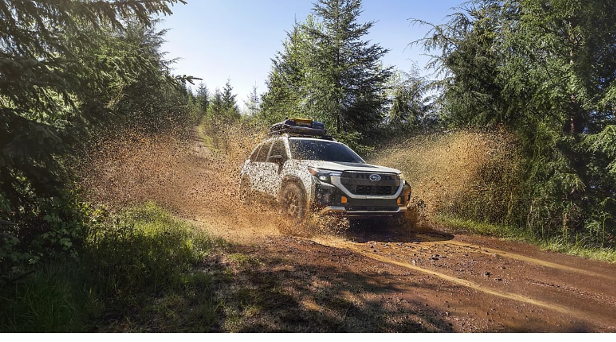 Rugged 2026 Subaru Forester with roof cargo carrier splashing through a deep mud puddle on a forest road near Arden and Mahwah, NJ, demonstrating standard Symmetrical All-Wheel Drive and Dual-Function X-MODE traction during heavy rain conditions.
