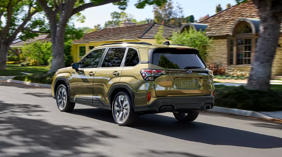 Rear three-quarter view of the 2026 Subaru Forester driving through a suburban residential neighborhood in Ridgewood, NJ, showcasing sleek rear LED taillights and standard Symmetrical All-Wheel Drive safety for local family commutes.