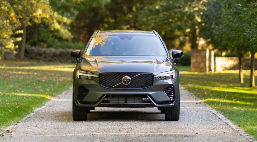 Front profile of a 2026 Volvo XC60 plug-in hybrid in Ramsey driving through a summer rainstorm on Route 17 showing its sleek athletic grille design