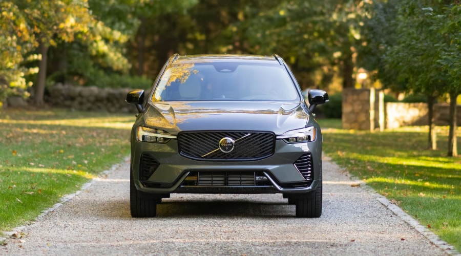 Front view of the 2026 Volvo XC60 Plug-in Hybrid parked on a scenic, tree-lined driveway during autumn in Ramsey, NJ, highlighting its electric all-wheel drive capability and wet road readiness for Bergen County drivers.