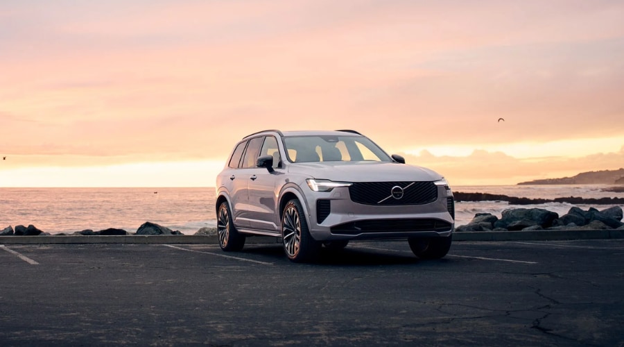 Front three-quarter view of the 2026 Volvo XC90 B6 Mild Hybrid in Platinum Grey parked by the coast at sunset, showcasing the perfect weekend getaway SUV available at our Volvo dealership in Ramsey NJ