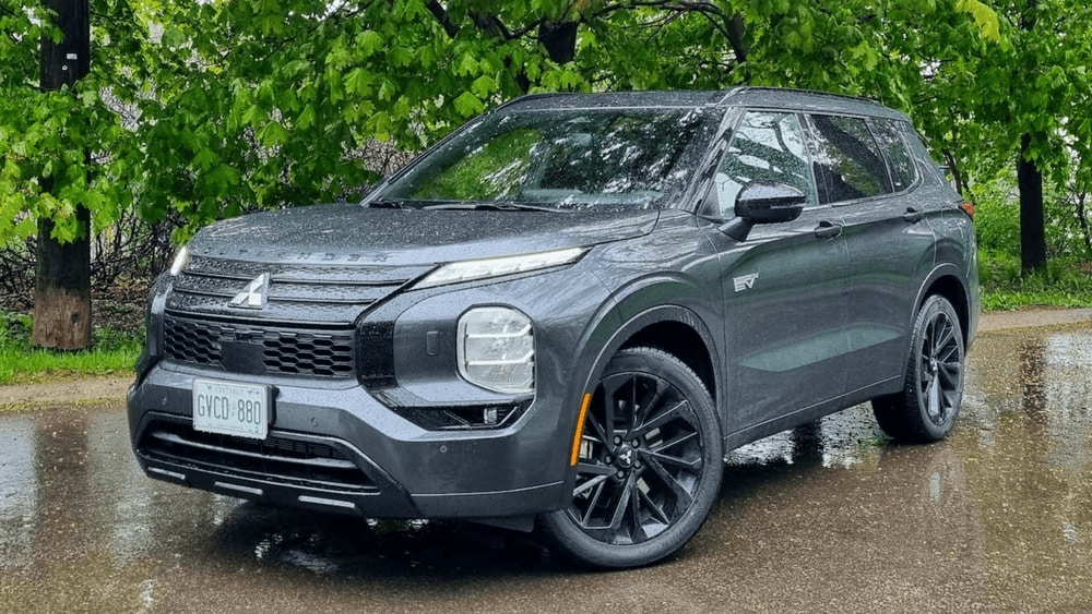 2025 Mitsubishi Outlander PHEV in dark gray parked on wet road surrounded by greenery, highlighting eco-friendly performance