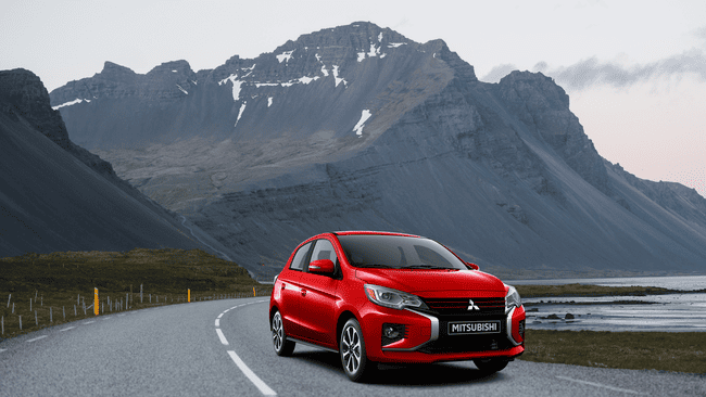 Red 2025 Mitsubishi Mirage compact car parked along scenic mountain road showcasing affordable value and style