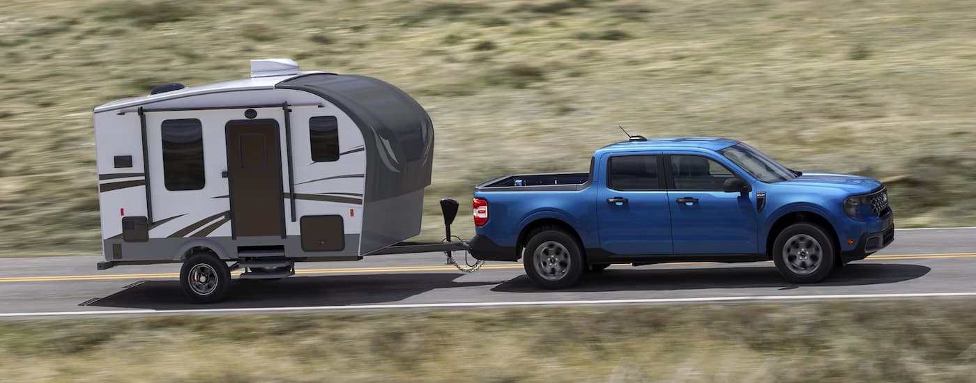 Blue 2025 Ford Maverick towing a camper trailer.