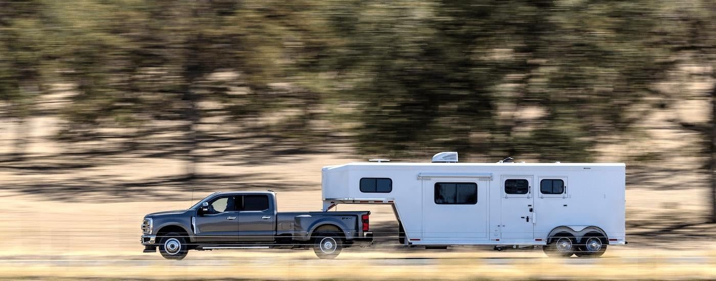 A gray 2023 Ford F-350 Lariat is shown towing a trailer.