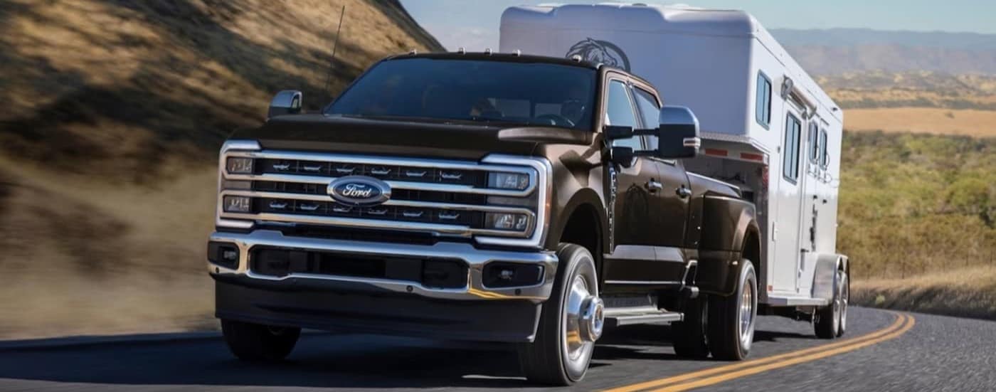 A black 2025 Ford F-350 Super Duty is shown towing a horse trailer on a highway.