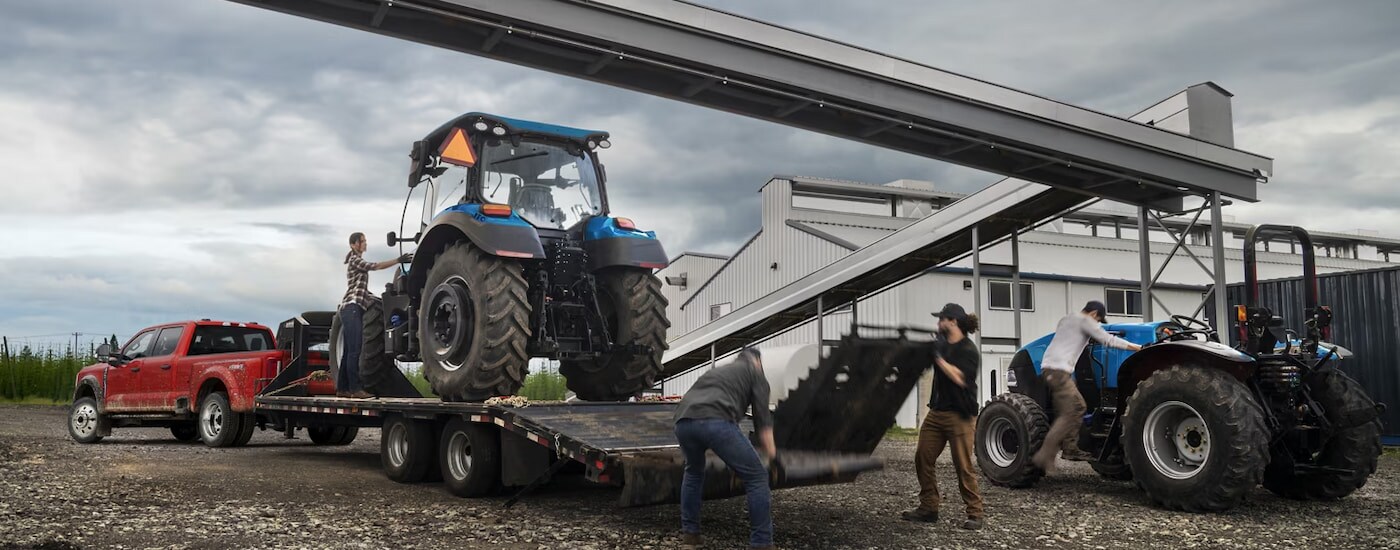 A red 2024 Ford F-450 XL Super Duty towing a tractor on a farm.