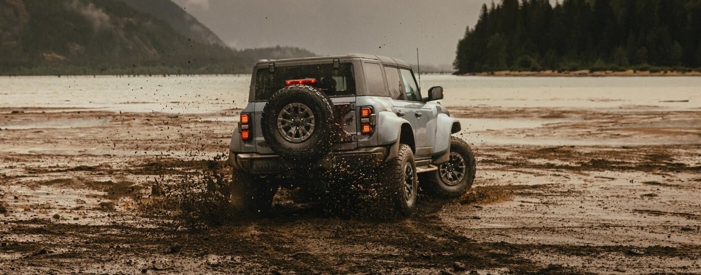 A grey 2024 Ford Bronco Raptor is shown kicking up mud off-road.