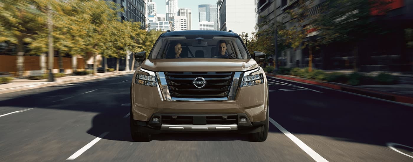 Brown 2023 Nissan Pathfinder driving on a city street to a used car dealer near Carey