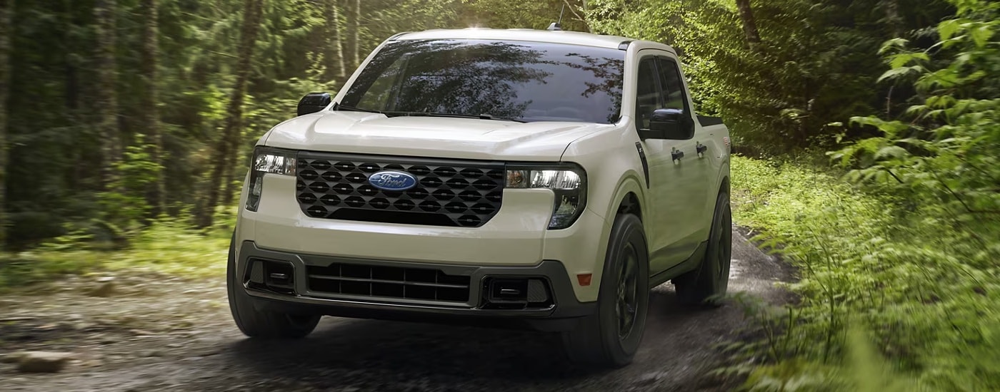 A white 2025 Ford Maverick XLT driving on a muddy wooded trail.