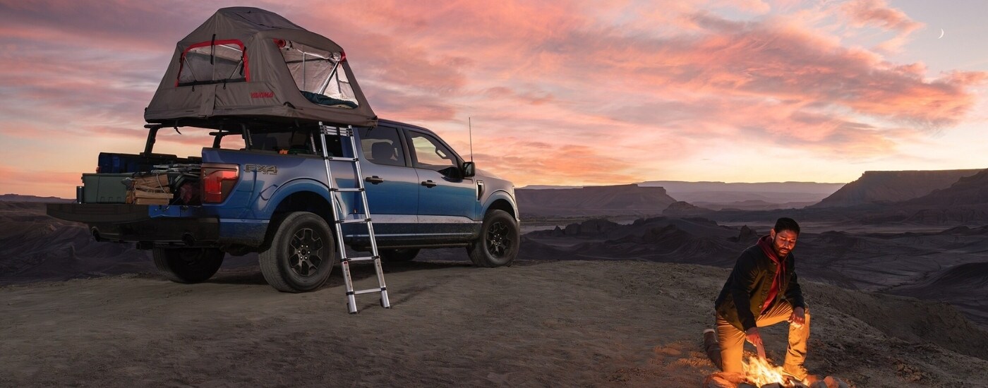 A blue 2025 Ford F-150 for sale in Findlay parked at a campsite with a pop-up tent in the bed.