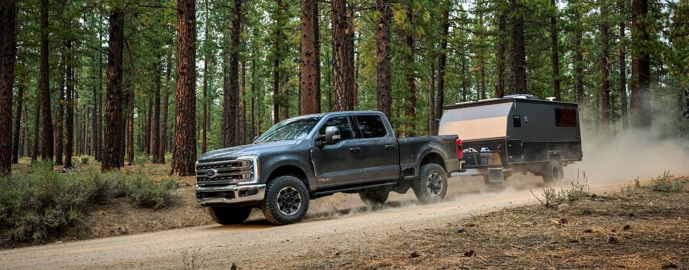 A grey 2024 Ford F-250 Tremor towing a small trailer off-road in the woods.