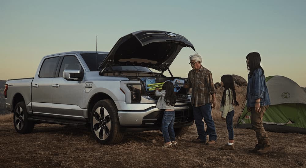 A family is getting camping gear out of the frunk of a silver 2023 Ford Lightning.