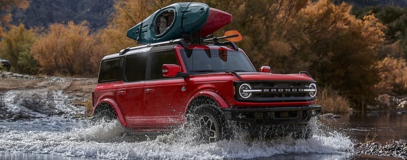A red 2023 Ford Bronco Outer Banks fording a shallow pond.